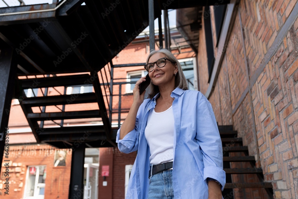 Fototapeta premium a mature gray-haired woman in a summer outfit walks around the city and chats on the phone