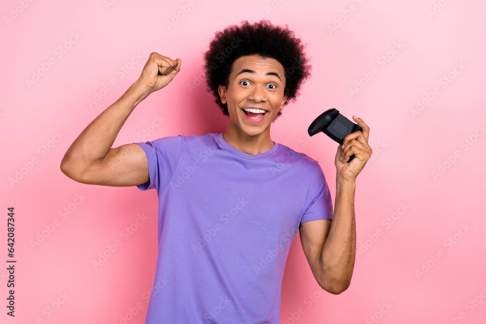 Photo of impressed man with afro hairstyle dressed blue t-shirt hold joystick raising fist win game isolated on pink color background Photo of impressed man with afro hairstyle dressed blue t-shirt hold joystick raising fist win game isolated on pink color background