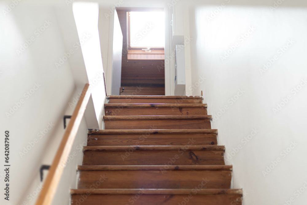 Un ancien escalier avec des marches en bois et une rambarde en bois, face à une porte ouverte qui baigne dans lumière Un ancien escalier avec des marches en bois et une rambarde en bois, face à une porte ouverte qui baigne dans lumière