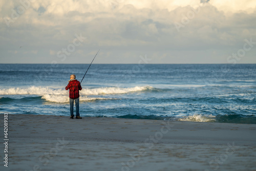 man beach fishing in the ocean waves at dusk