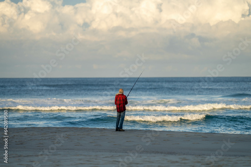 man beach fishing in the ocean waves at dusk