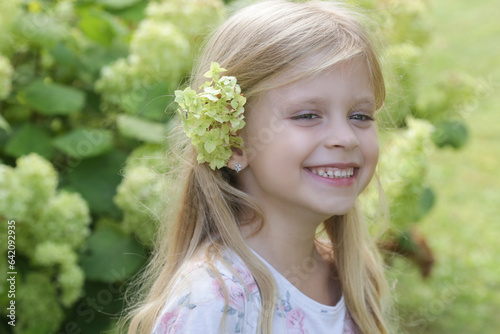 Candid outdoor portrait of happy little girl with green flower behind her ear