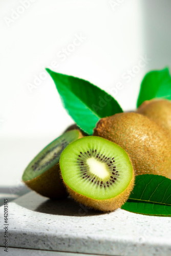 Ripe kiwi fruits in sunlight. Heap of whole kiwi fruits with green leaves and fresh cut kiwi on table. Healthy organic fruits full of vitamins and antioxidants.