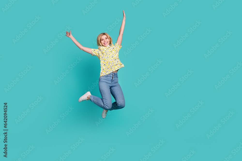 Full length photo of cheerful excited girl dressed yellow print t-shirt jumping high empty space isolated teal color background