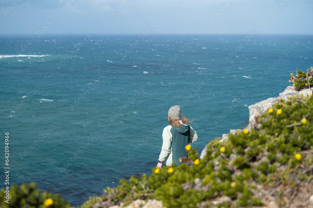 Woman standing on a rock onto of a cliff looking out at the view of the ocean Woman standing on a rock onto of a cliff looking out at the view of the ocean