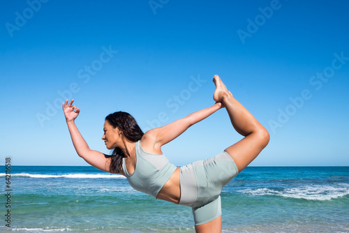 Athletic woman in standing yoga pose with ocean in background