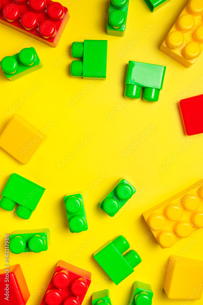 Naklejka premium Children's plastic multi-colored constructor on yellow background, top view. Game for children, toddlers, building blocks, bricks, toys, child development, co-creation. Flat lay