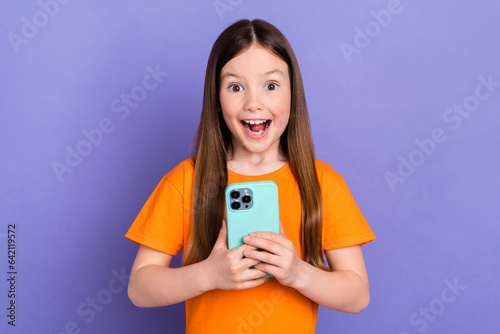 Photo of small beautiful preschool girl childhood hold smartphone shocked reaction eshop entertainment isolated on violet color background