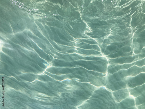 Light blue, ripped, clear and transparent sea water with sun glare 