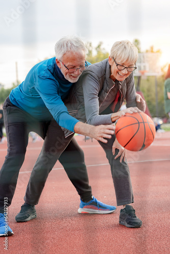 Cheerful active senior couple playing basketball on the urban basketball street court. Happy living after 60. © lordn