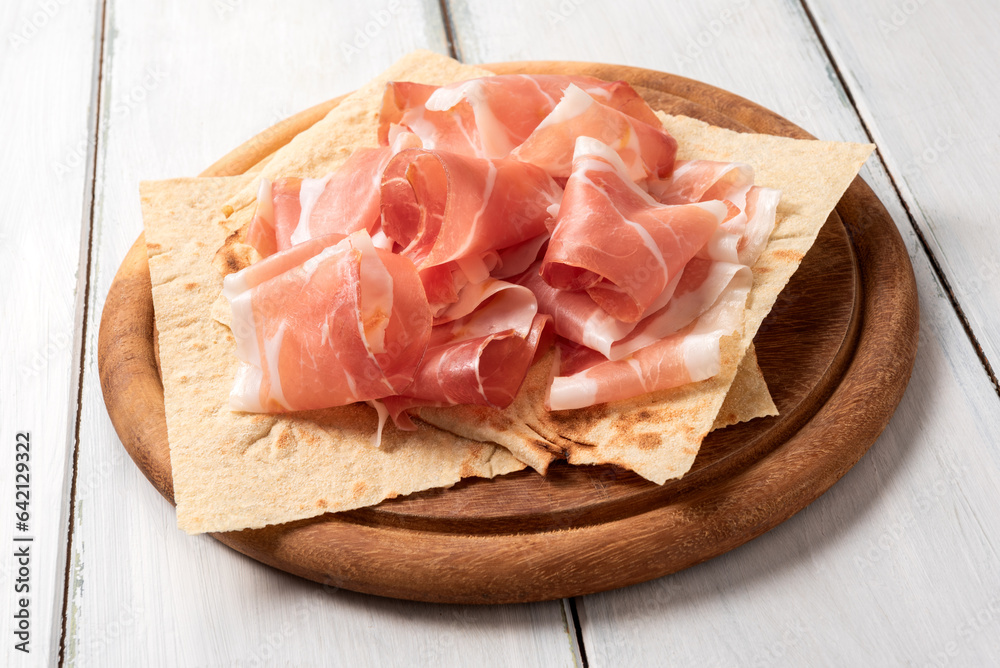Fette di prosciutto crudo su pane carasau e tagliere in legno, cibo rustico italiano Fette di prosciutto crudo su pane carasau e tagliere in legno, cibo rustico italiano