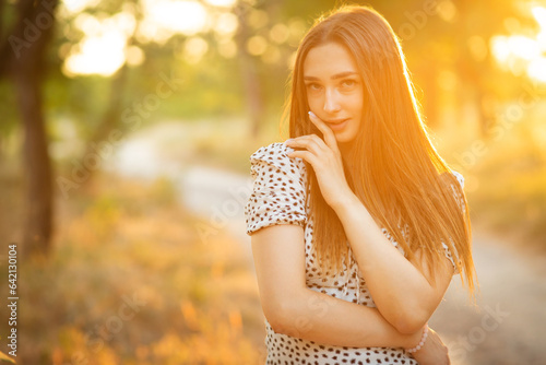 cute smiling girl lit by warm sunlight on a path looking at you  young romantic woman in a dress walking at sunset in a forest planting