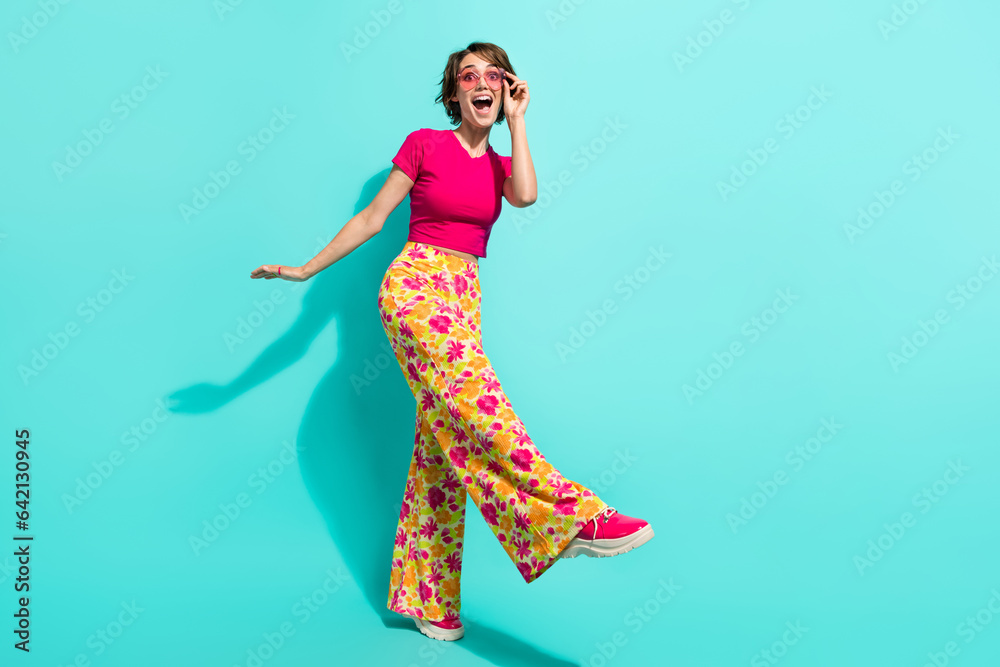 Full length photo of cute impressed woman dressed flower print trousers having fun empty space isolated teal color background Full length photo of cute impressed woman dressed flower print trousers having fun empty space isolated teal color background
