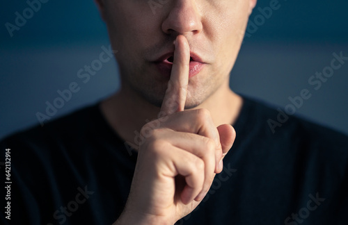 Secret and silence. Quiet silent shh gesture with finger on lips. Man doing expression with hand on mouth. Taboo topic, censorship or freedom or speech. Conspiracy theory. Confidential talk. photo