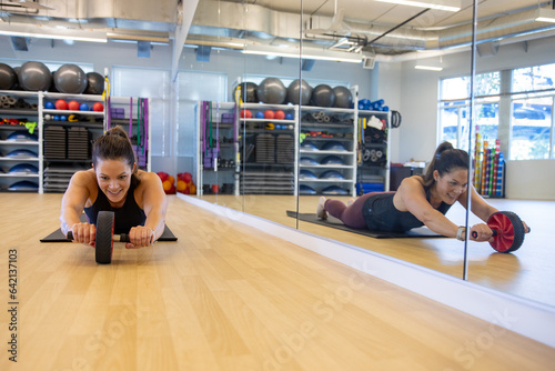 Strong, physically fit woman working out in gym with ab roller. Strengthening her abdominal core muscles with wheel equipment.  photo