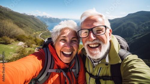 Active senior caucasian couple hiking in mountains with backpacks, enjoying their adventure doing selfie