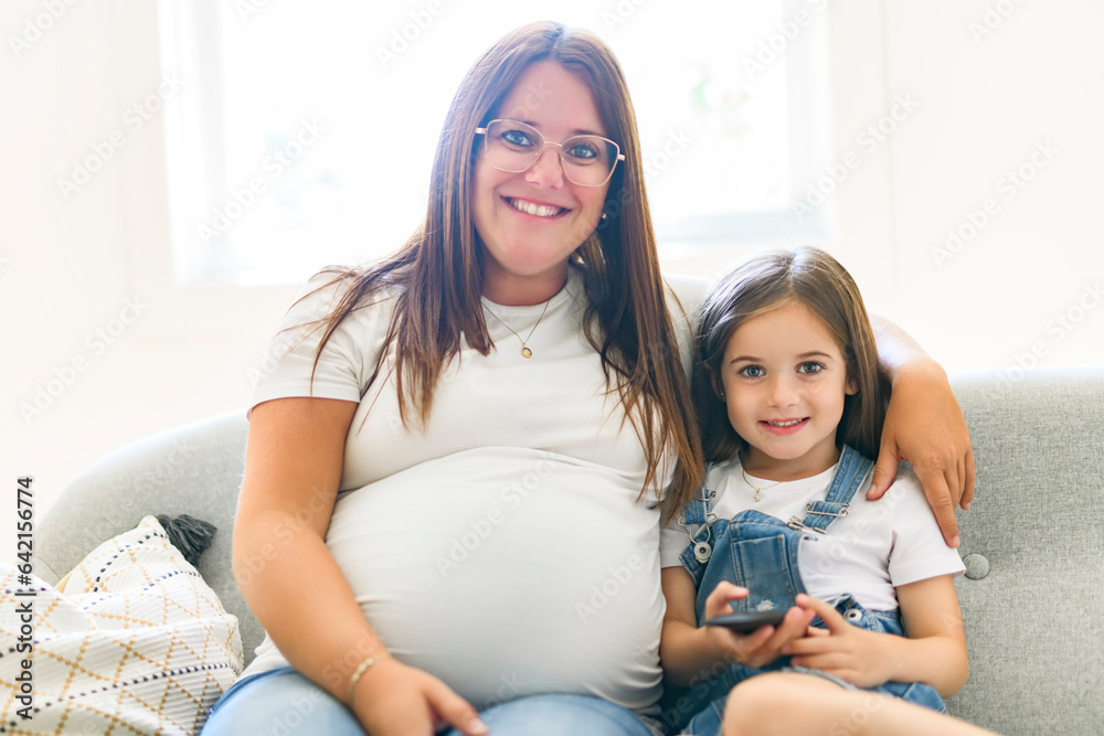 Excited little daughter touching pregnant mom tummy, standing next to