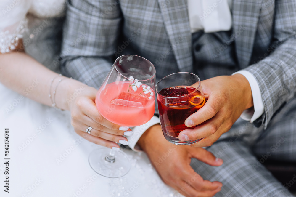 The bride and groom hold glass glasses with an alcoholic cocktail in their hands, whiskey in their hands at a party. Wedding photography, portrait. The bride and groom hold glass glasses with an alcoholic cocktail in their hands, whiskey in their hands at a party. Wedding photography, portrait.