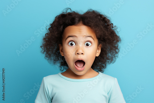 Studio portrait of a surprised preschool girl on a blue background.