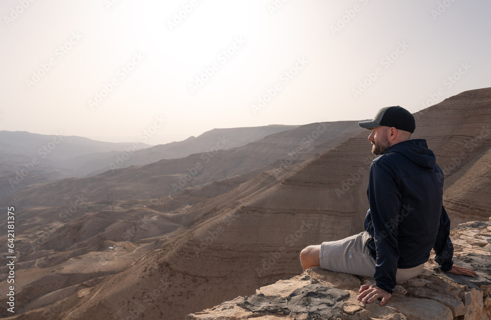Tourist man with cap sit in viewpoint landscape of wilderness Canyon Wadi Mujib in Jordan