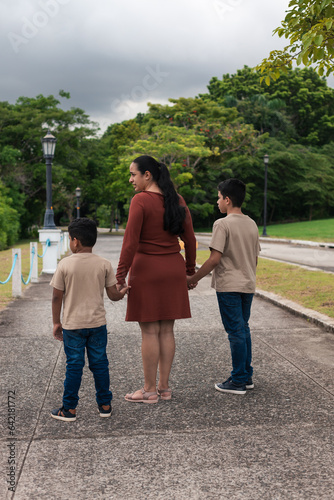 Latina mom holds her children's hands, wearing a khaki sweater © Dionisio