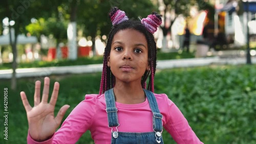 An African-American girl with pink braids acts like a doll on a city street.Slow motion.	
