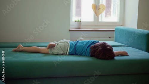 Bored child lying on couch with nothing to do, restless little boy grounded at home struggles with boredom photo