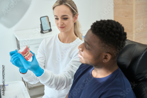 Woman doctor showing model of teeth to man