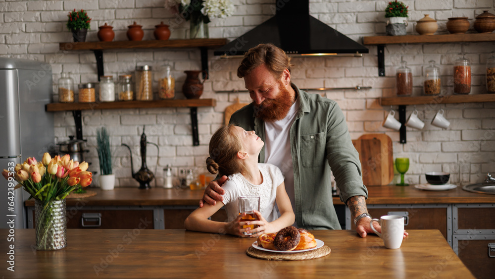 Positive parent hugging child near drinks and pastry in kitchen in morning Positive parent hugging child near drinks and pastry in kitchen in morning