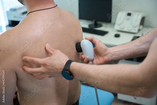 Physiotherapist treating adult man for dorsodynia with ultrasonic device photo