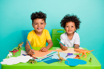 Full body photo of cute two little boys friends sitting table playing learning dressed stylish clothes isolated on cyan color background