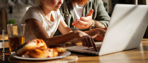 Banner image of tattooed father sitting near daughter using laptop and pastry in kitchen in morning