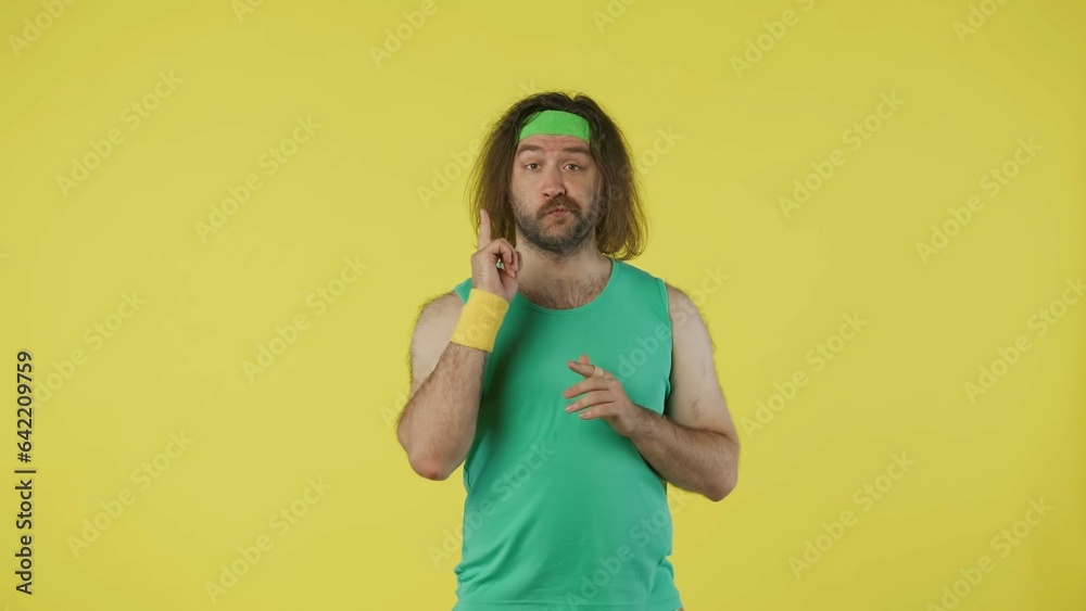 Man in green top and headband thinking about something, pointing finger. Isolated on yellow background. Man in green top and headband thinking about something, pointing finger. Isolated on yellow background.