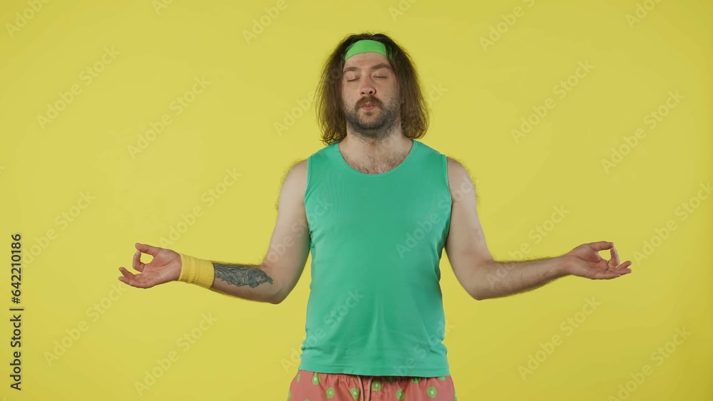 Man in green top and headband holding hands in meditative position. Isolated on yellow background. Man in green top and headband holding hands in meditative position. Isolated on yellow background.