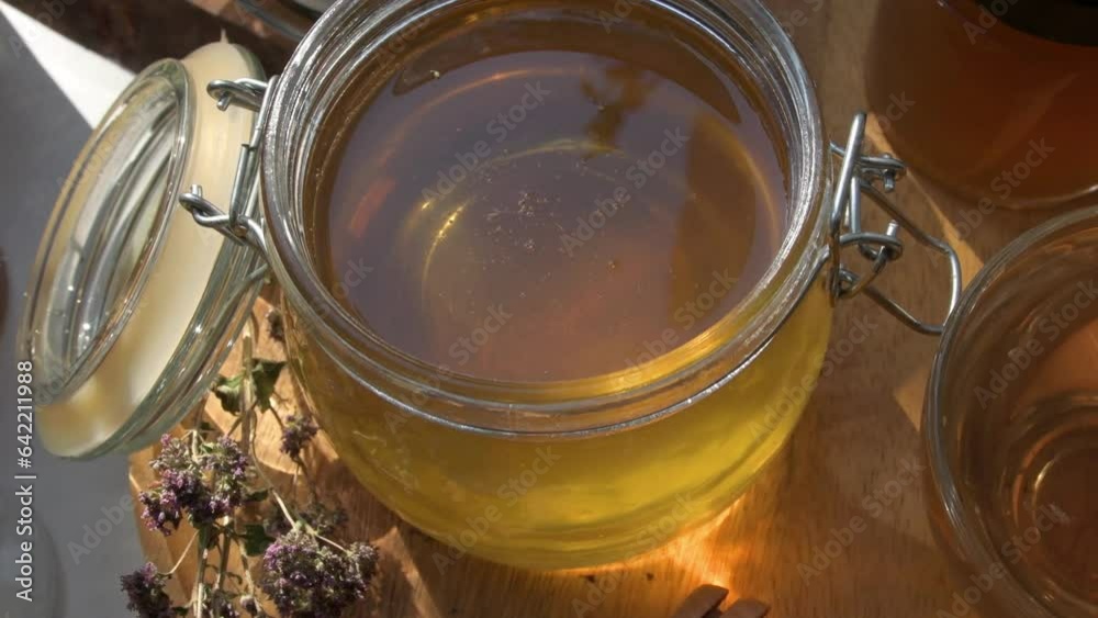 beautiful fresh natural golden linden honey in big glass jar at wooden tray with sunny light inside. close up beautiful fresh natural golden linden honey in big glass jar at wooden tray with sunny light inside. close up