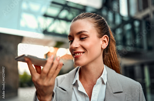 Foto Portrait of a beautiful confident smiling adult professional woman standing against the background of a business center holding a phone and dictating a plan, reminders, questions in the application