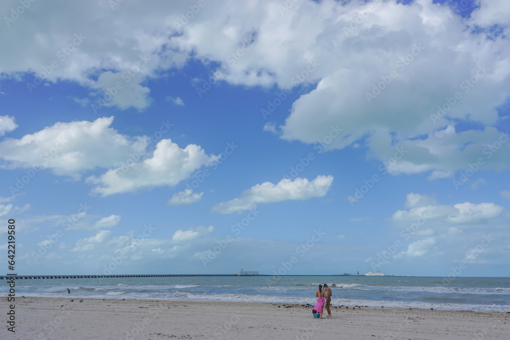 Progreso, Yucatan, Mexico: A young couple standing on a  beach on the Gulf of Mexico; a cruise ship at the end of a long pier in the distance.