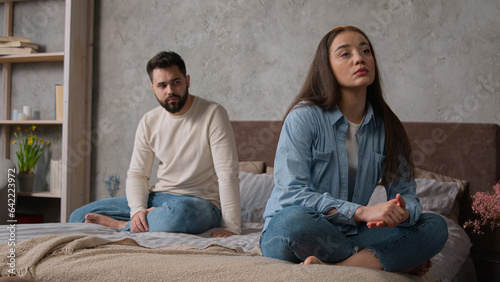 Sad annoyed Caucasian couple family spouses sit apart on bed offended man and woman relationship problem. Husband wife silence after conflict argue misunderstanding breakup divorce quarrel in bedroom photo