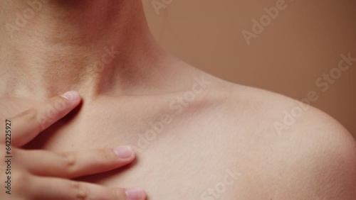 Young attractive woman with clean skin gently touches her naked shoulder with her own hand close up on a brown background. Concept of skin care for health and beauty