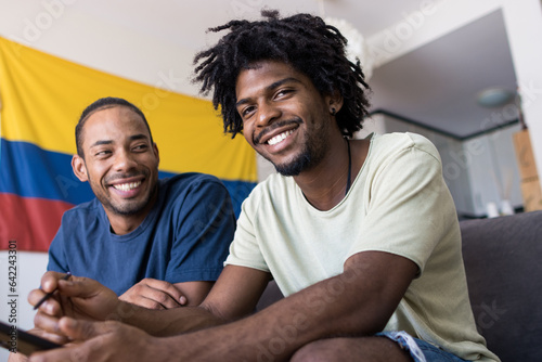 Two afro american friends on the sofa at home with the Colombian flag in the background.