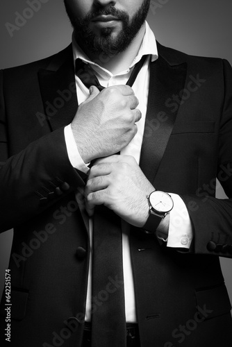 Tela Bearded man tightening tie on grey background, closeup