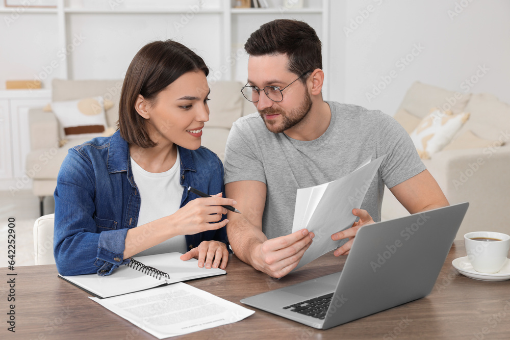 Young couple with papers discussing pension plan at wooden table indoors Young couple with papers discussing pension plan at wooden table indoors