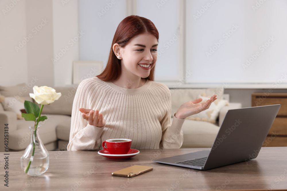 Happy woman having video chat via laptop at wooden table in room