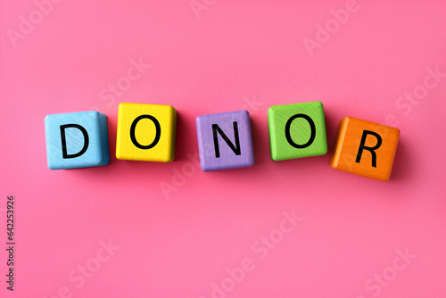 Word Donor made of colorful wooden cubes on pink background, flat lay