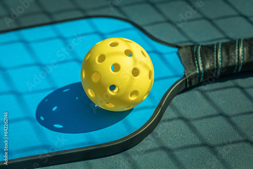 Blue Pickleball paddle with yellow Pickleball with shadow of Pickleball net.