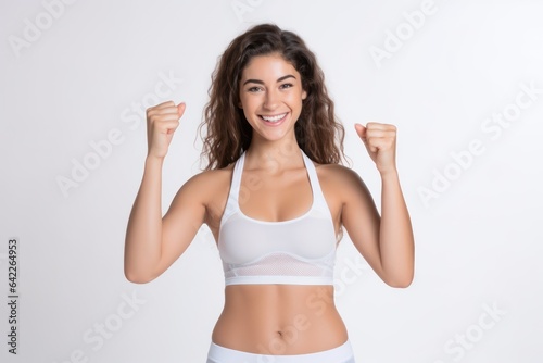 Portrait of a smiling sportswoman in white sportswear showing her thumb up and her biceps isolated on a white background and Looking at the camera.