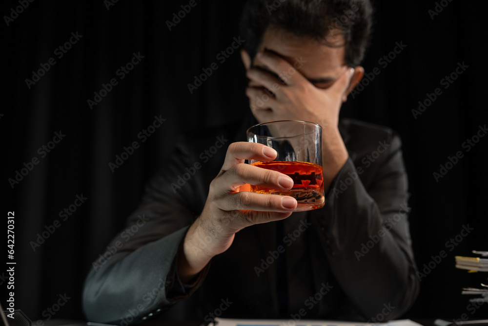 Asian businessman stressed at work failed business problem paperwork Desperate man holding a glass of alcohol Sitting at the desk late at night in the office Depressed and hopeless concept.