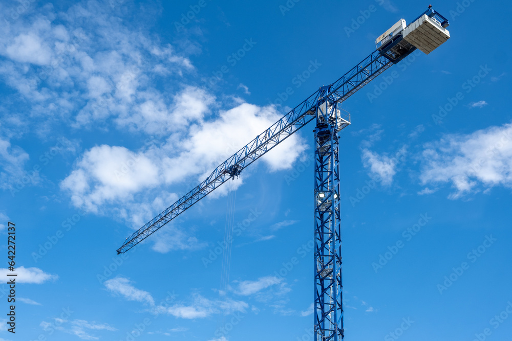 A crane and a building under construction against a blue sky background. Builders work on large construction sites, and there are many cranes working in the field of new construction. A crane and a building under construction against a blue sky background. Builders work on large construction sites, and there are many cranes working in the field of new construction.