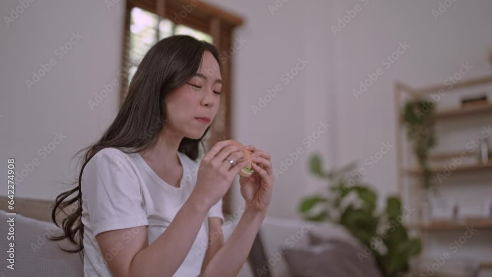 Young hungry Asian woman eating junk food hamburger have lunch fast food at home, showing diet food choices. Young hungry Asian woman eating junk food hamburger have lunch fast food at home, showing diet food choices.