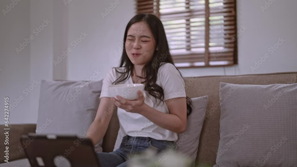 Asian woman eats snacks and watching funny film on portable tablet ,unhealthy lifestyle concept. Asian woman eats snacks and watching funny film on portable tablet ,unhealthy lifestyle concept.